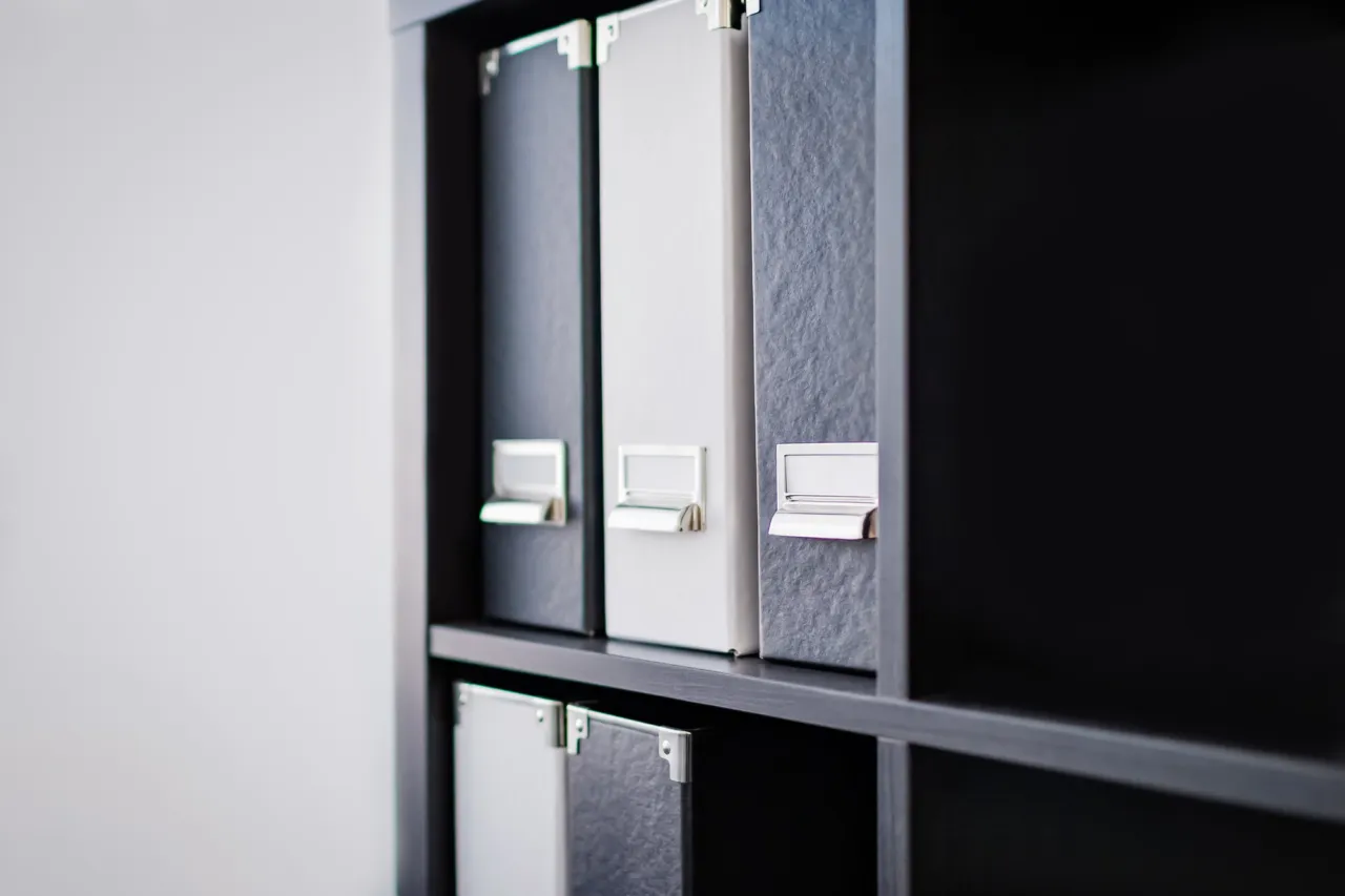 Three labelled compliance binders on a navy shelf in an Isle of Man office