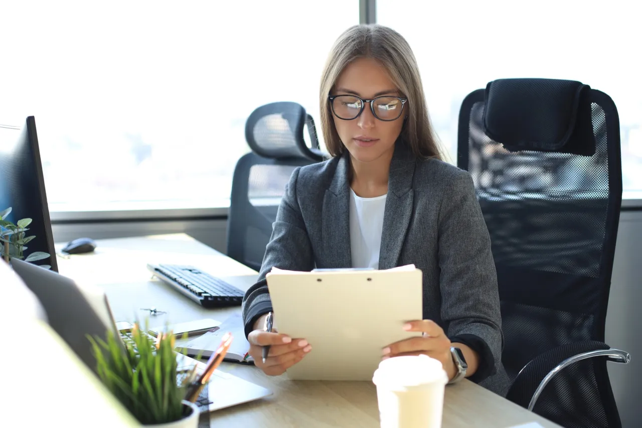 A compliance officer reviewing customer relationship files at a desk in an Isle of Man office