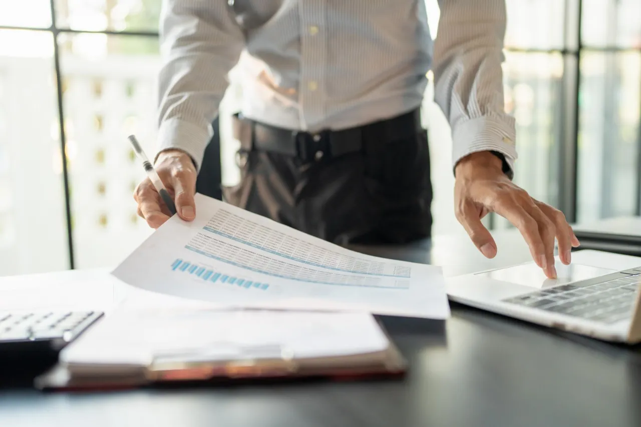 Two people reviewing a printed report and figures together at an office desk