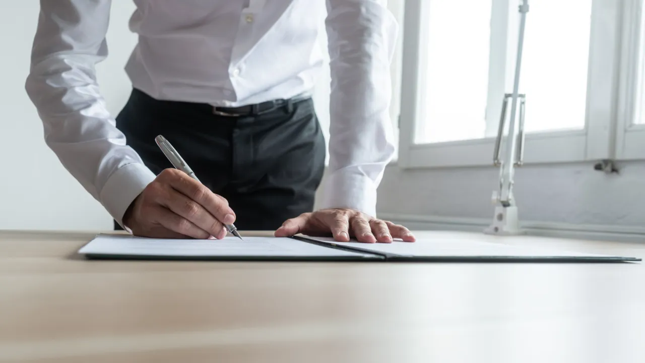 A man standing at his desk signing a document with a fountain pen
