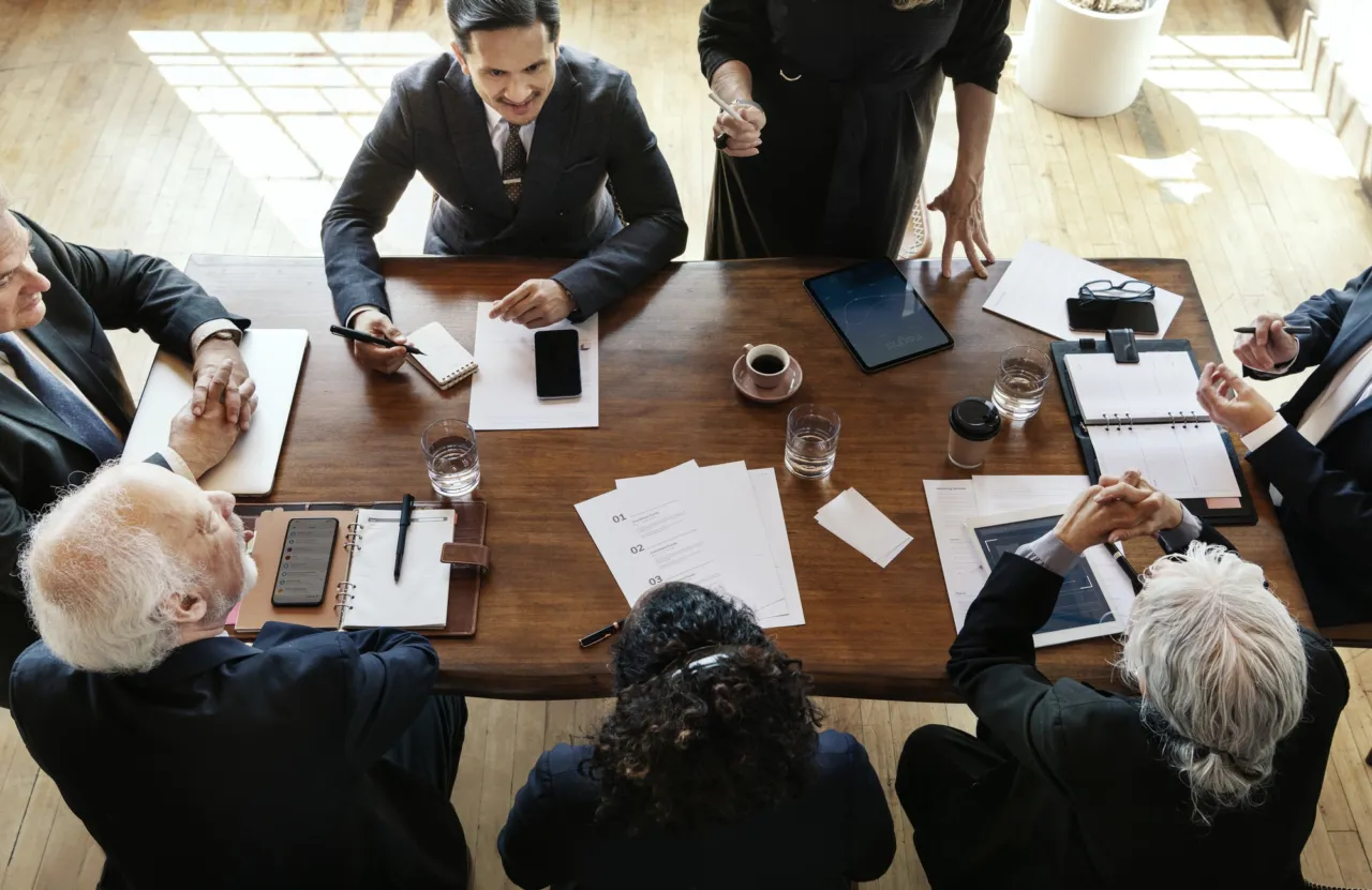An overhead view of a board meeting with papers spread across the table