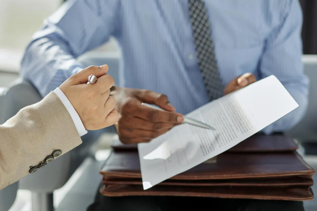 One person handing a signed document across a desk to another