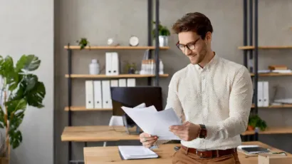 A man reading a document in an office lined with ring binders