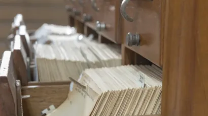 A wooden index card cabinet with one drawer open, holding records