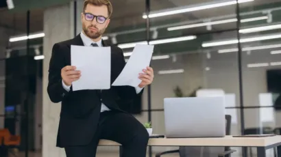 A man in a suit comparing two documents in a modern office
