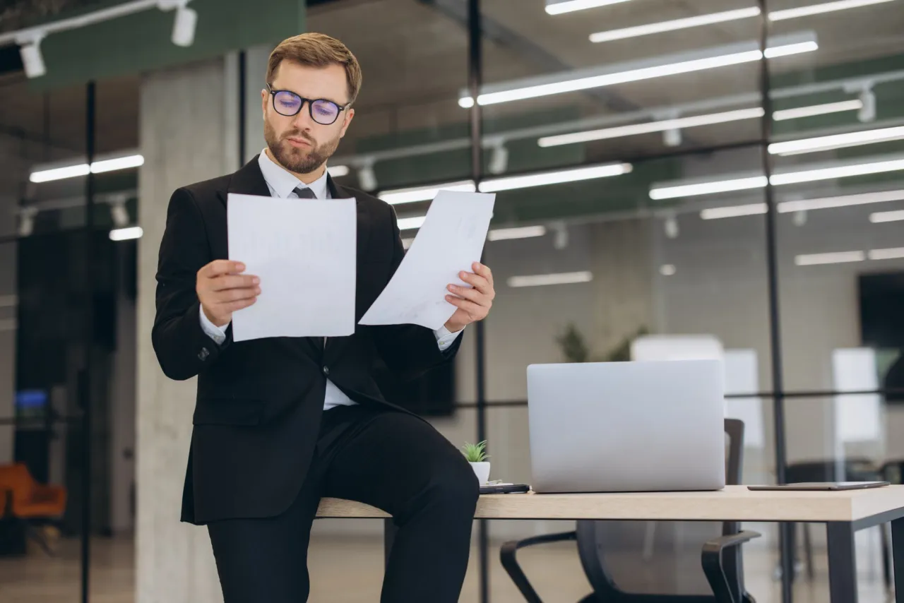 A man in a suit comparing two documents in a modern office